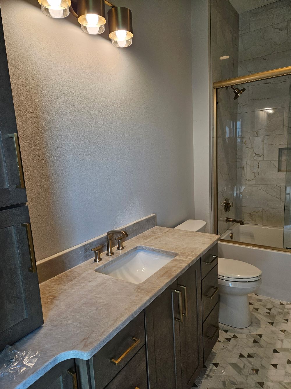 Finished bathroom with quartzite vanity top, brushed gold fixtures, and tiled tub shower