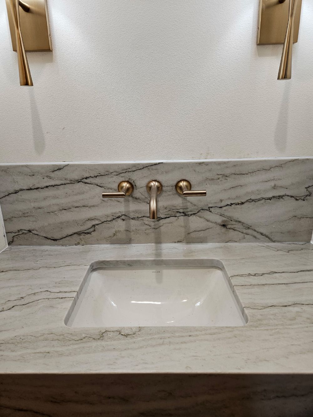 Wall-mounted brushed gold faucet over undermount sink in quartzite counter and backsplash