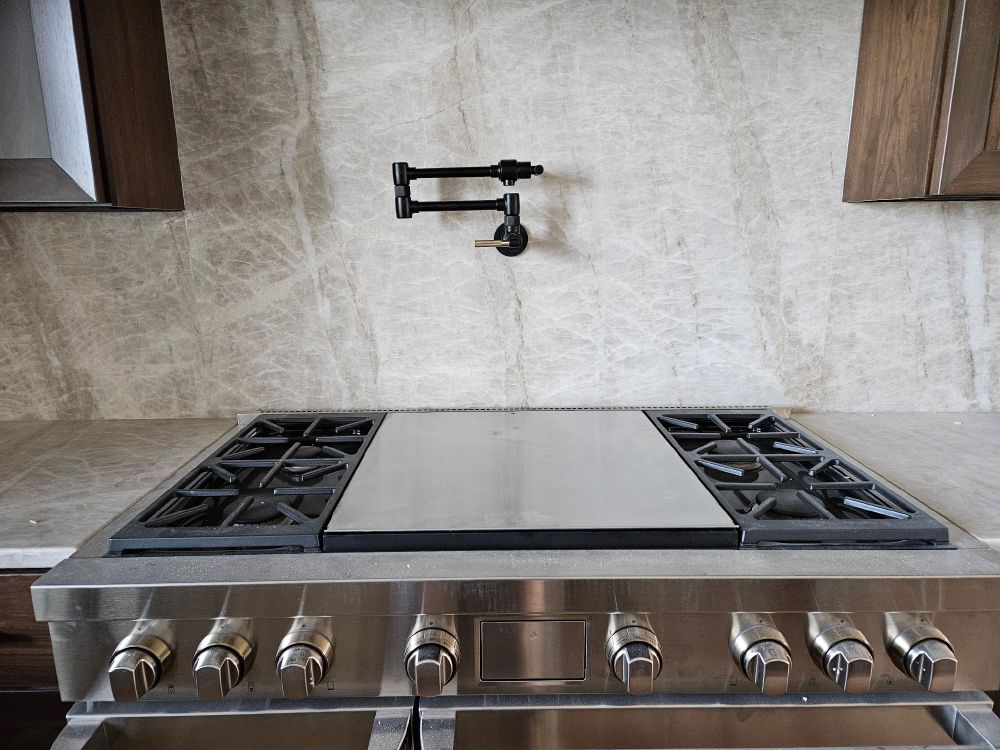 Matte black wall-mount pot filler over a stainless range top